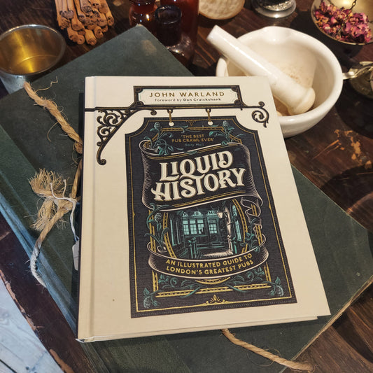 A copy of the book Liquid History lying on an old hardback book wrapped in string next to a pestle and mortar, herbs and other apothecary tools