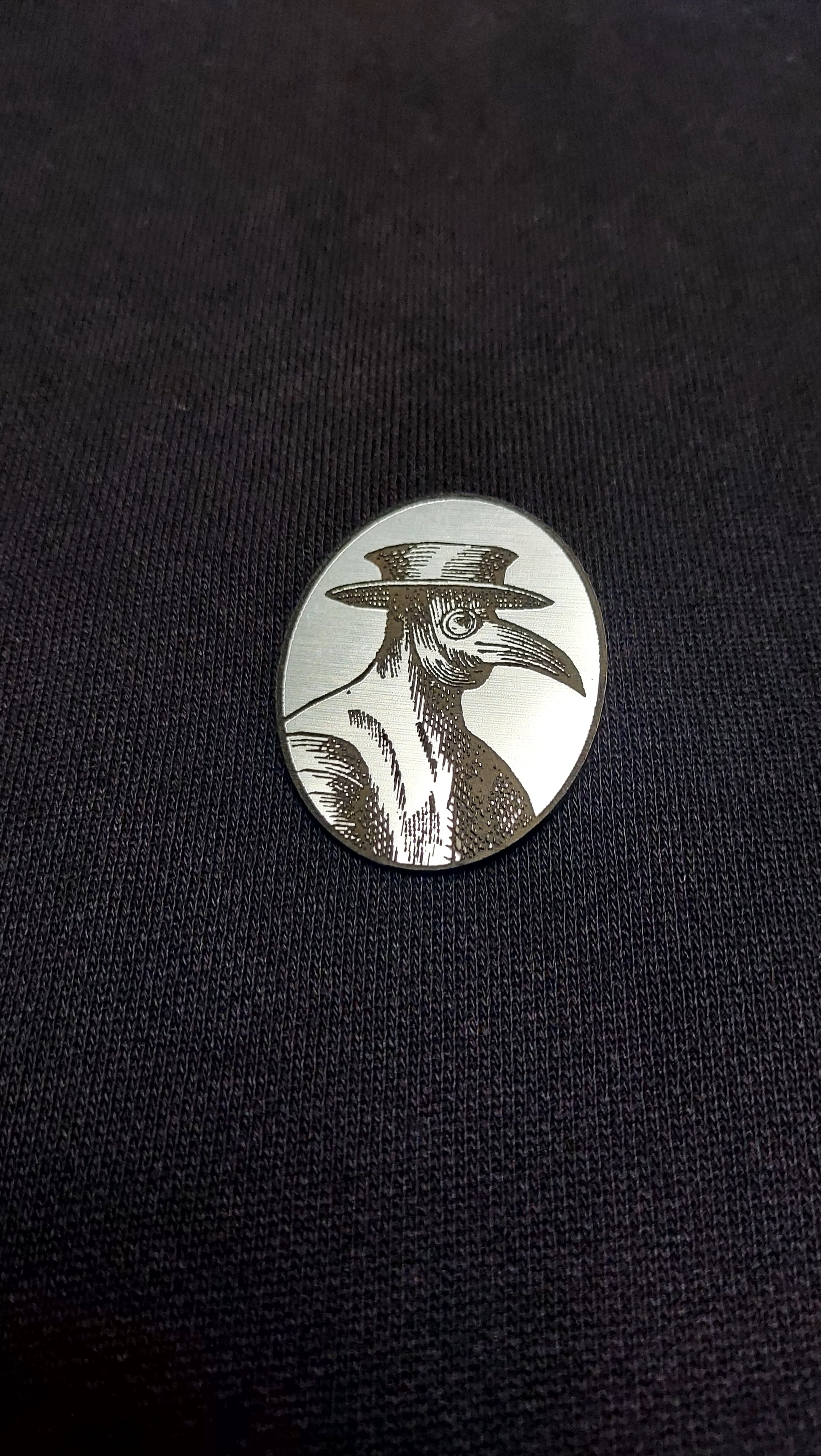 A brooch with the silver plague doctor design on black fabric
