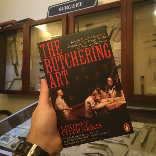The book The Butchering Art held up in from of the museum's collection of surgical instruments