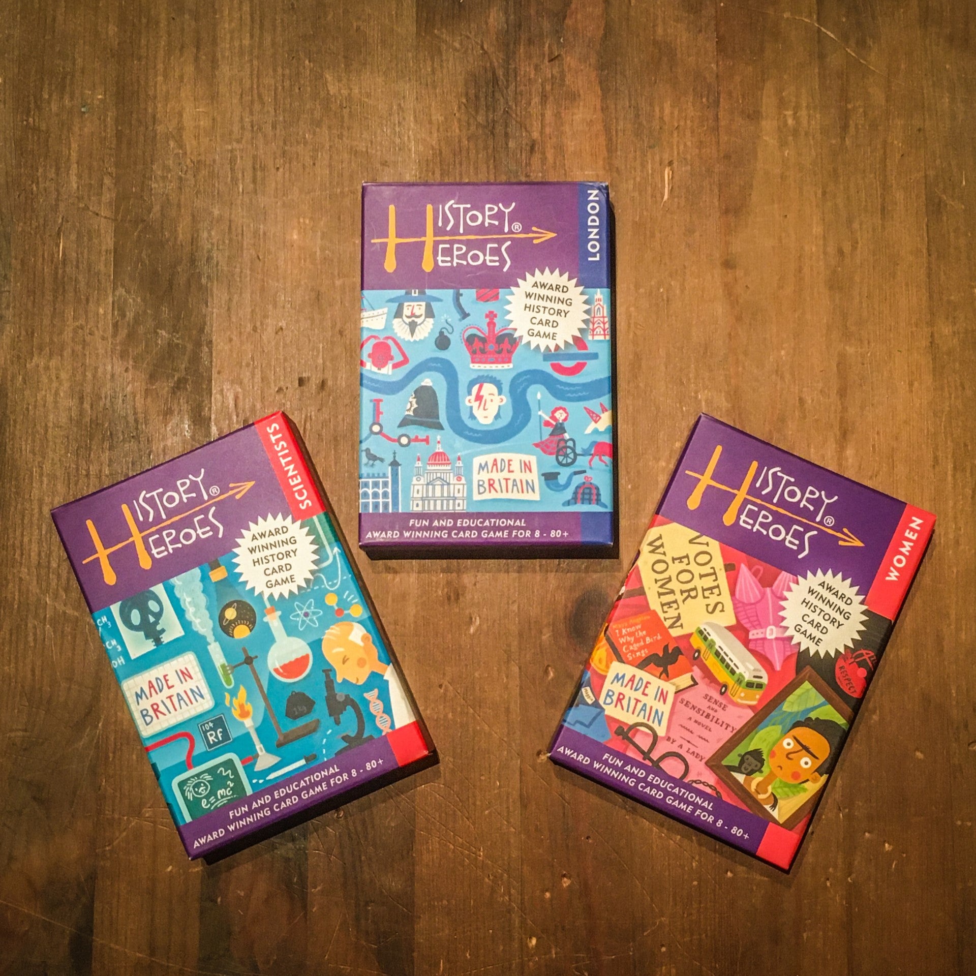 Three History Heroes game boxes on a wooden surface: Scientists, London, Women