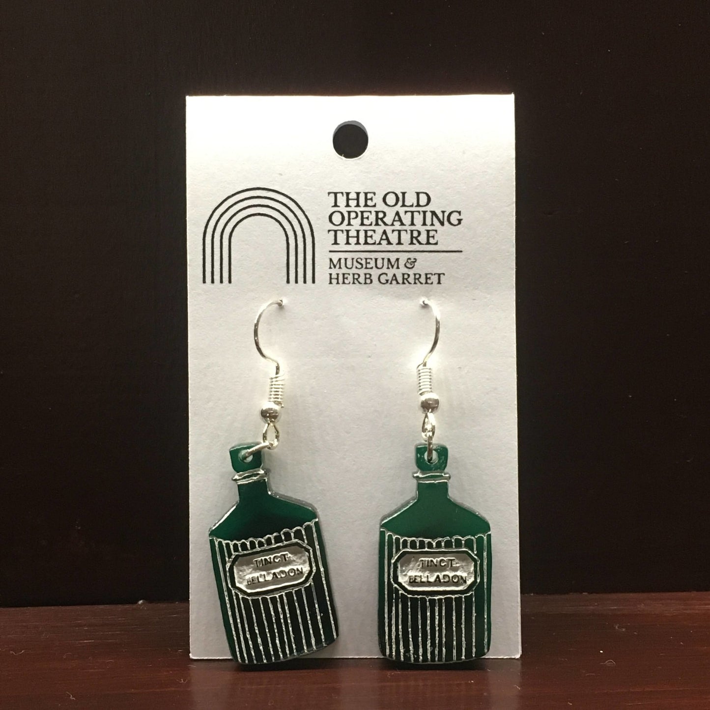 Pair of green dangle earrings in the shape of a bottle with the label 'tinct. belladon'