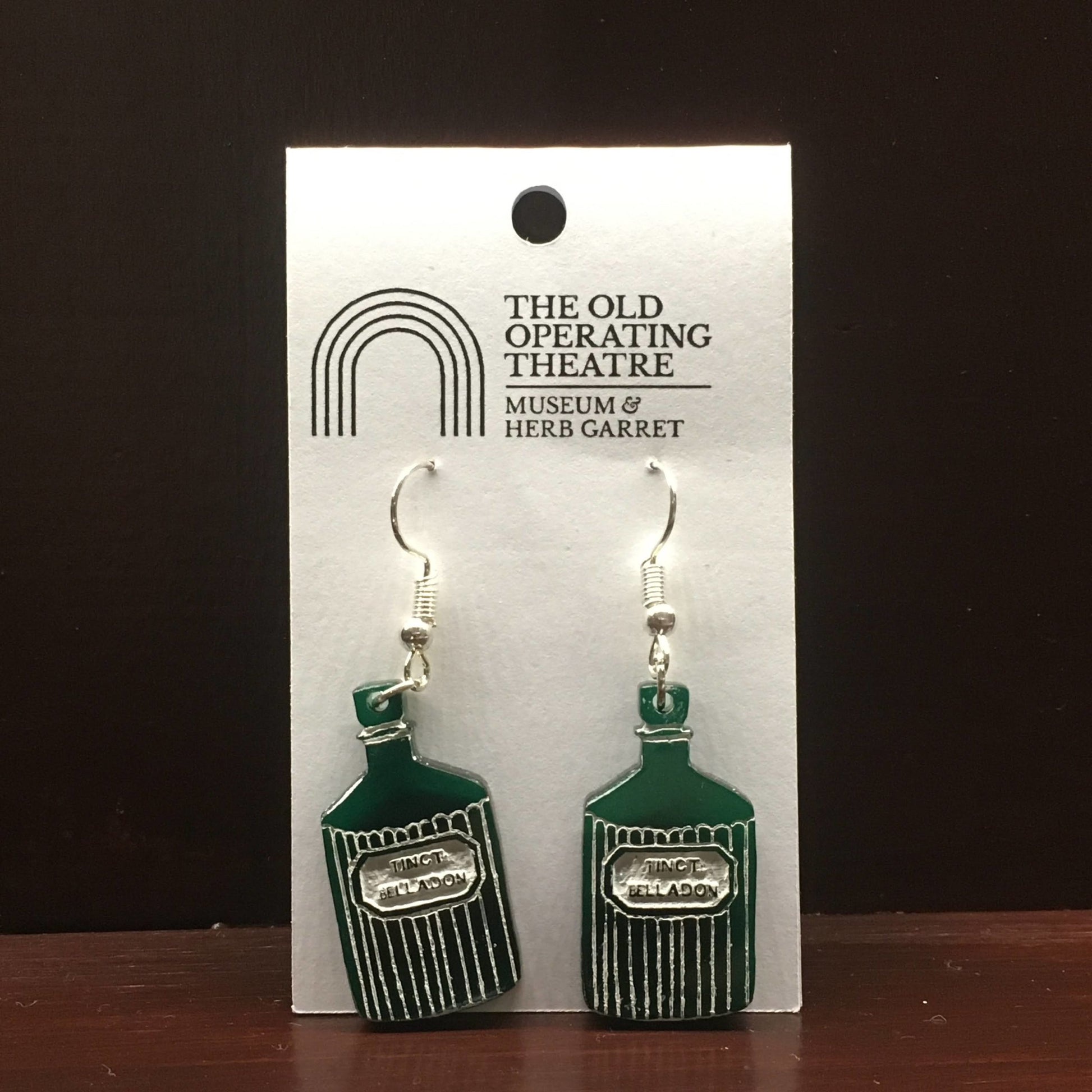 Pair of green dangle earrings in the shape of a bottle with the label 'tinct. belladon'