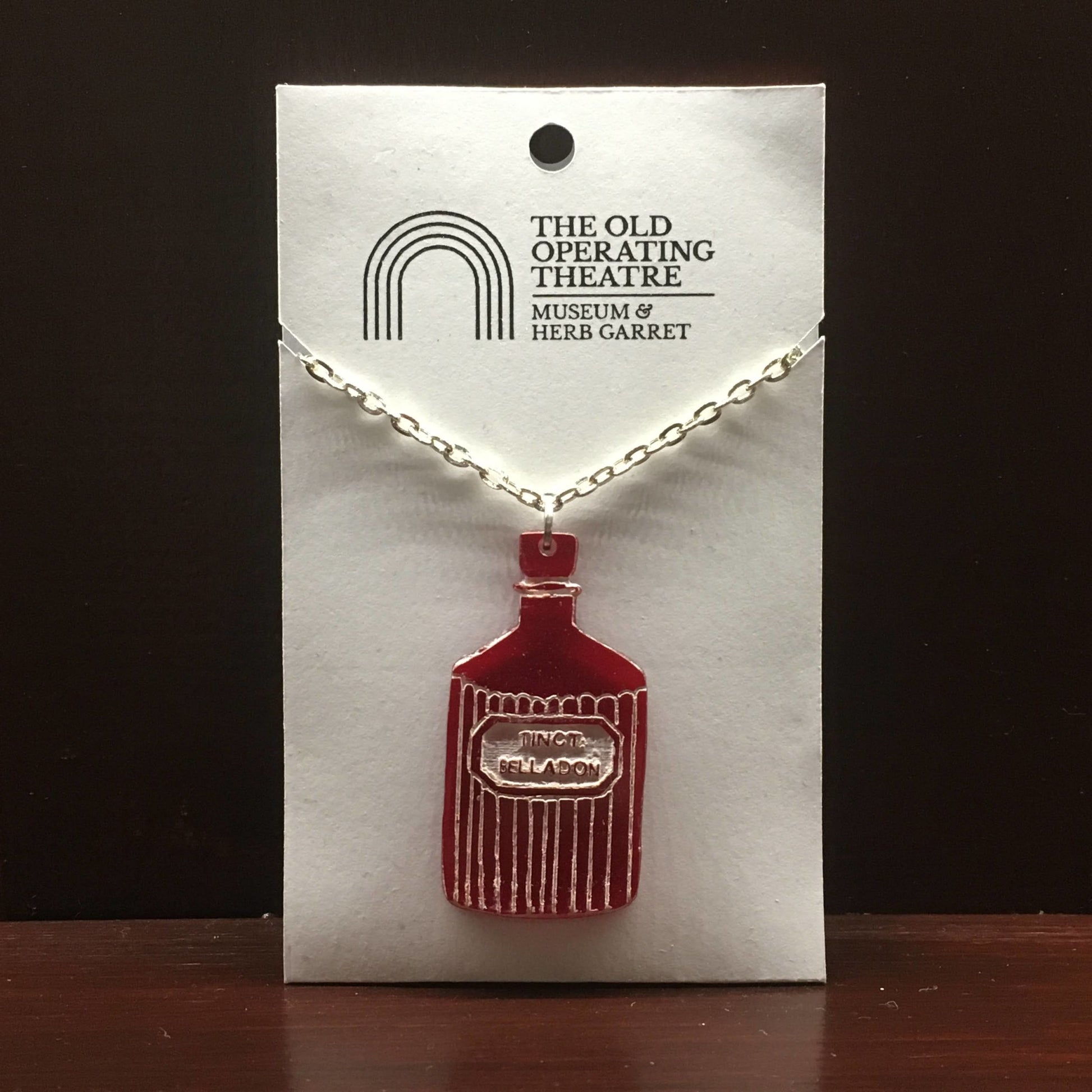 Red pendant in the shape of a bottle with the label 'tinct. belladon'