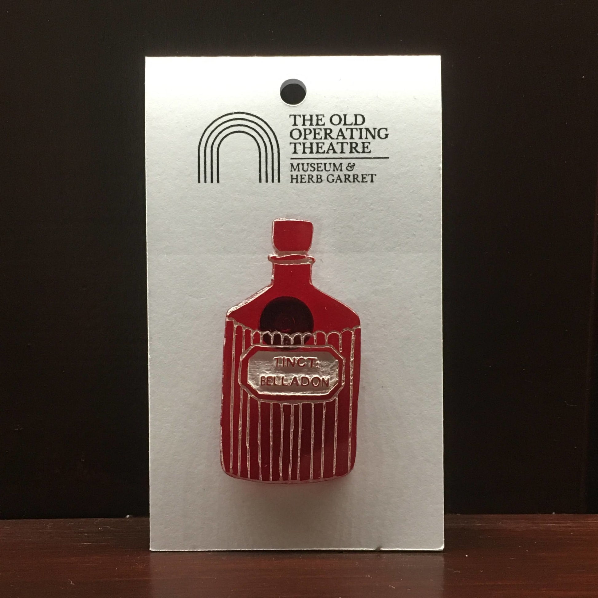 Red brooch in the shape of a bottle with the label 'tinct. belladon'