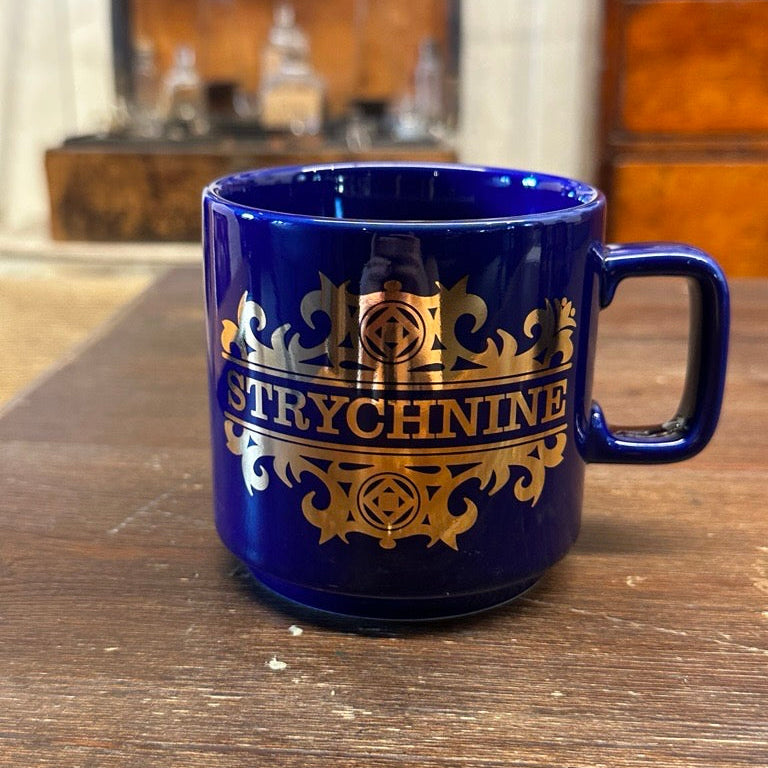Blue mug with gold 'Strychnine' text on a wooden surface