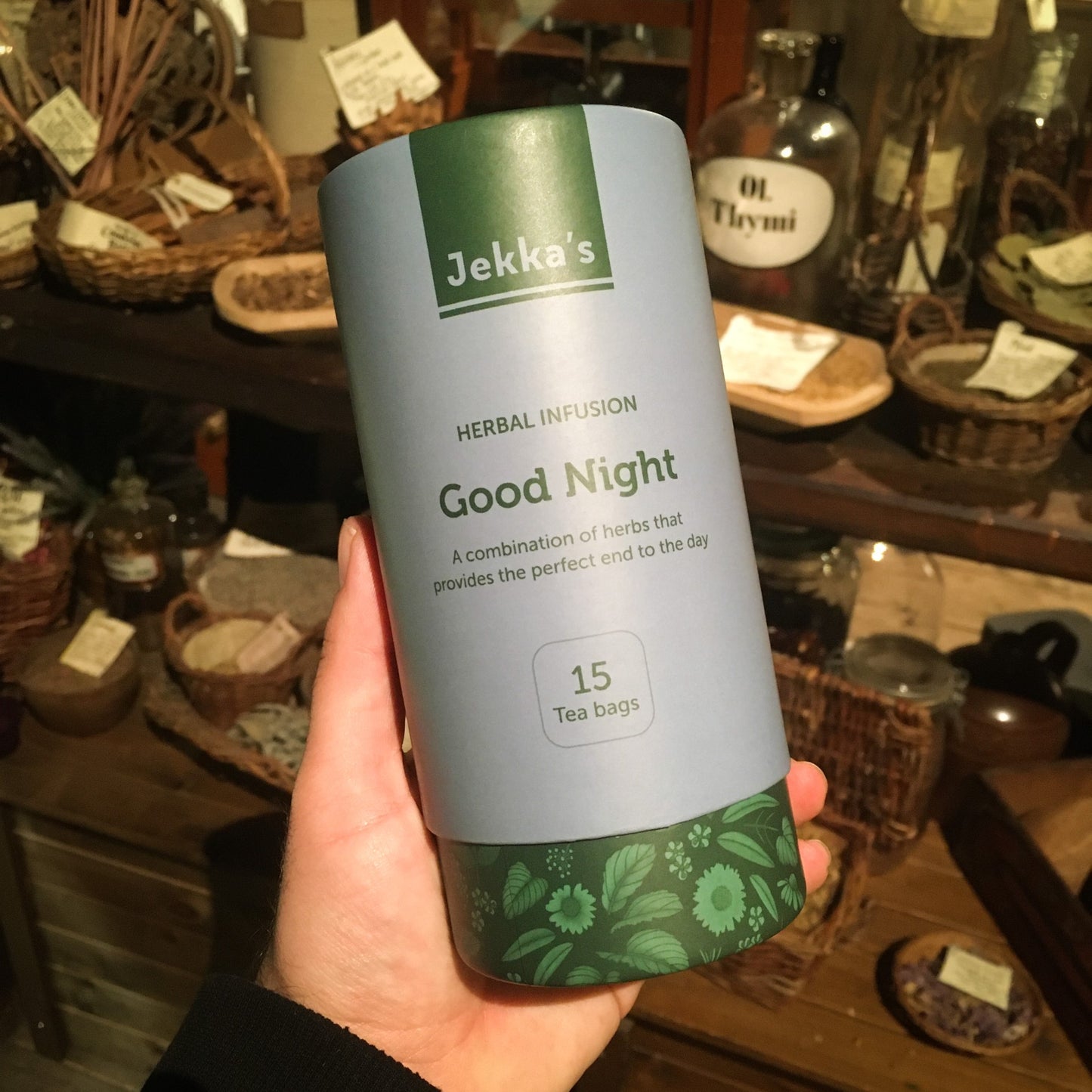 A blue and green cardboard tube of Good Night herbal infusion being held up in the museum's herb garret