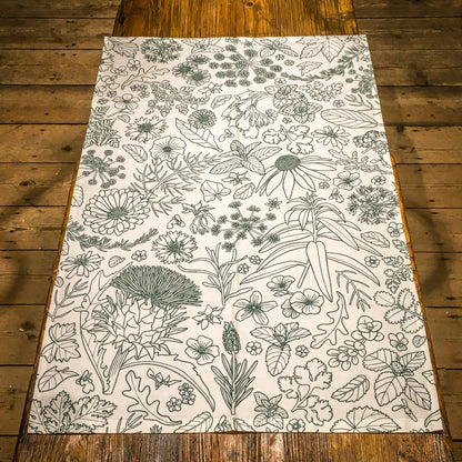 The tea towel, decorated in green outline with flowers and leaves, laid out on the old operating table