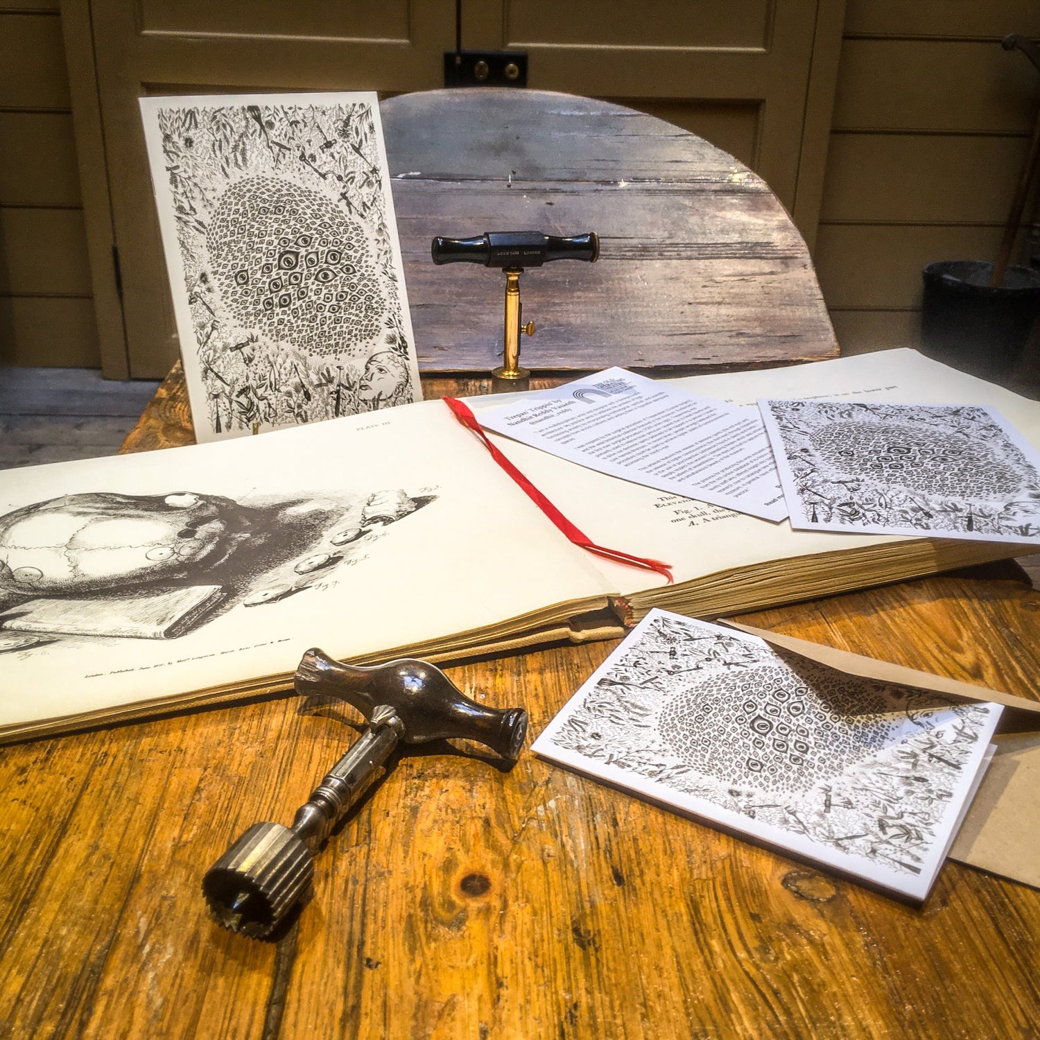Prints and a greeting card featuring the trephination design, placed next to a trephine and a large book illustrating trephination