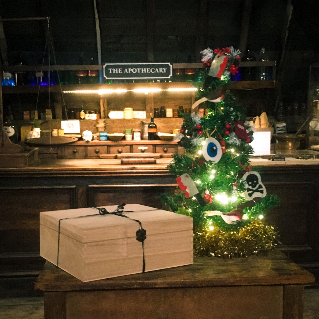 A wooden box next to a small Christmas tree decorated with skulls, eyes and cleavers, placed on a wooden table by the apothecary counter in the museum