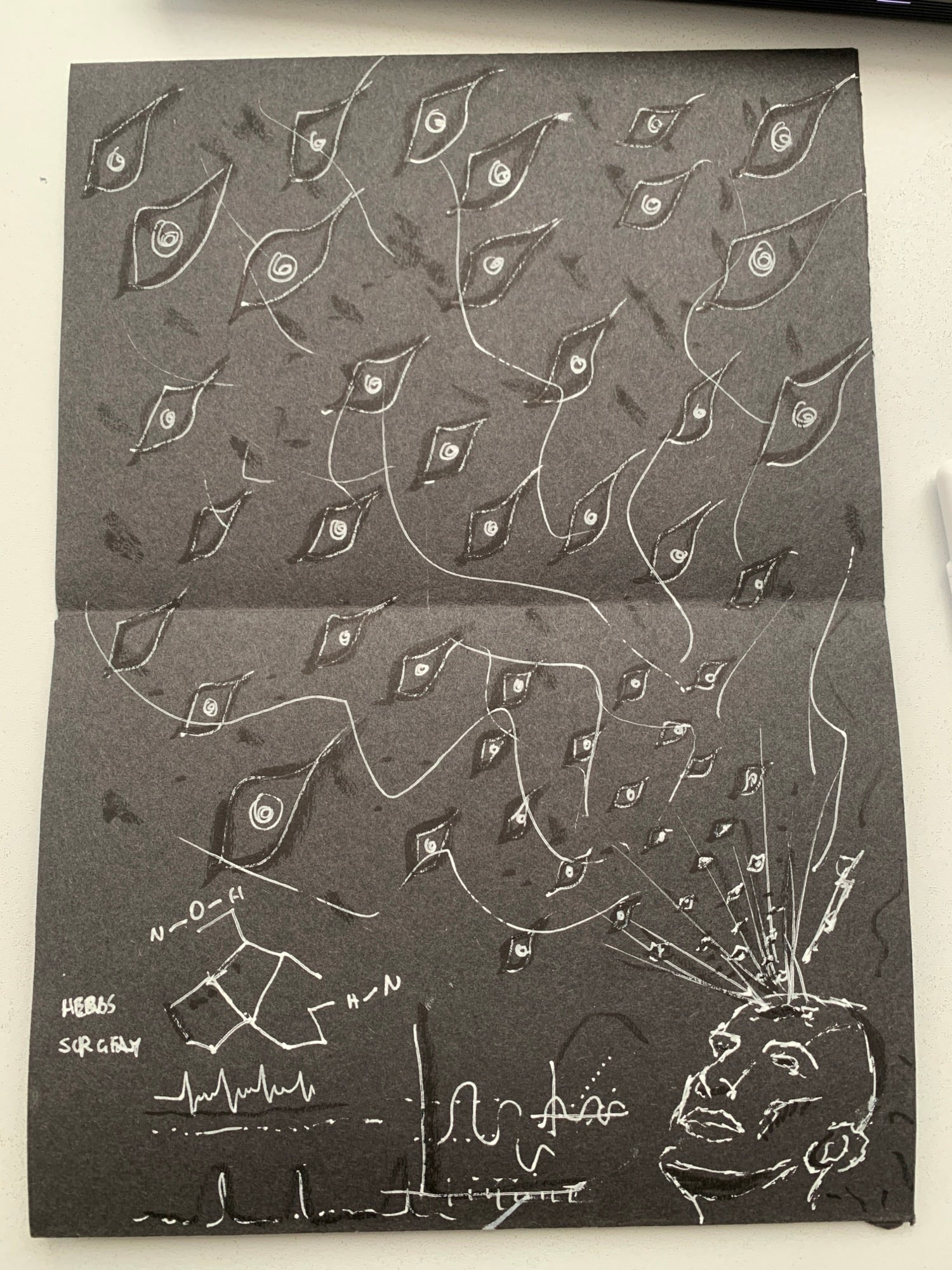 Drawing in white on black paper of a head in the bottom right corner with eyes emanating from it