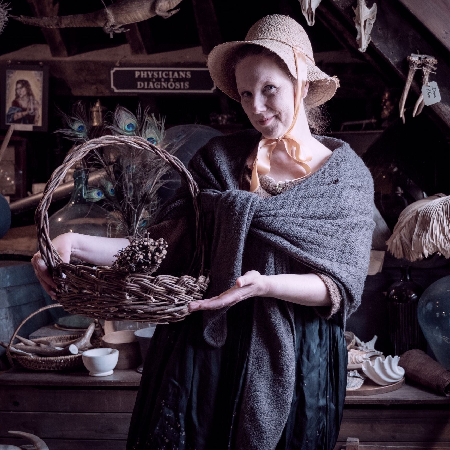 A woman wearing a shawl and bonnet holds up a wicker basket within the museum's herb garret