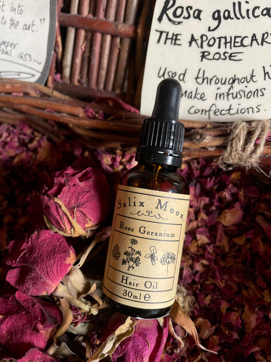 A bottle of Salix Moon Rose Geranium hair oil, on dried rose petals in a basket
