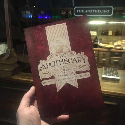Red and white notebook with illustrations of jars and text: The Apothecary. A Guide to Tinctures, ointments and cure alls