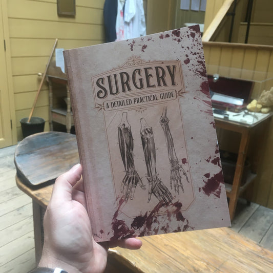 Notebook with illustrations of arm anatomy and blood spatter. Text: Surgery a detailed practice guide