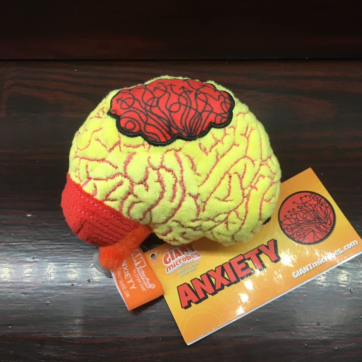 Yellow plush toy in the shape of a brain with a red cloud on its surface, on a wooden shelf