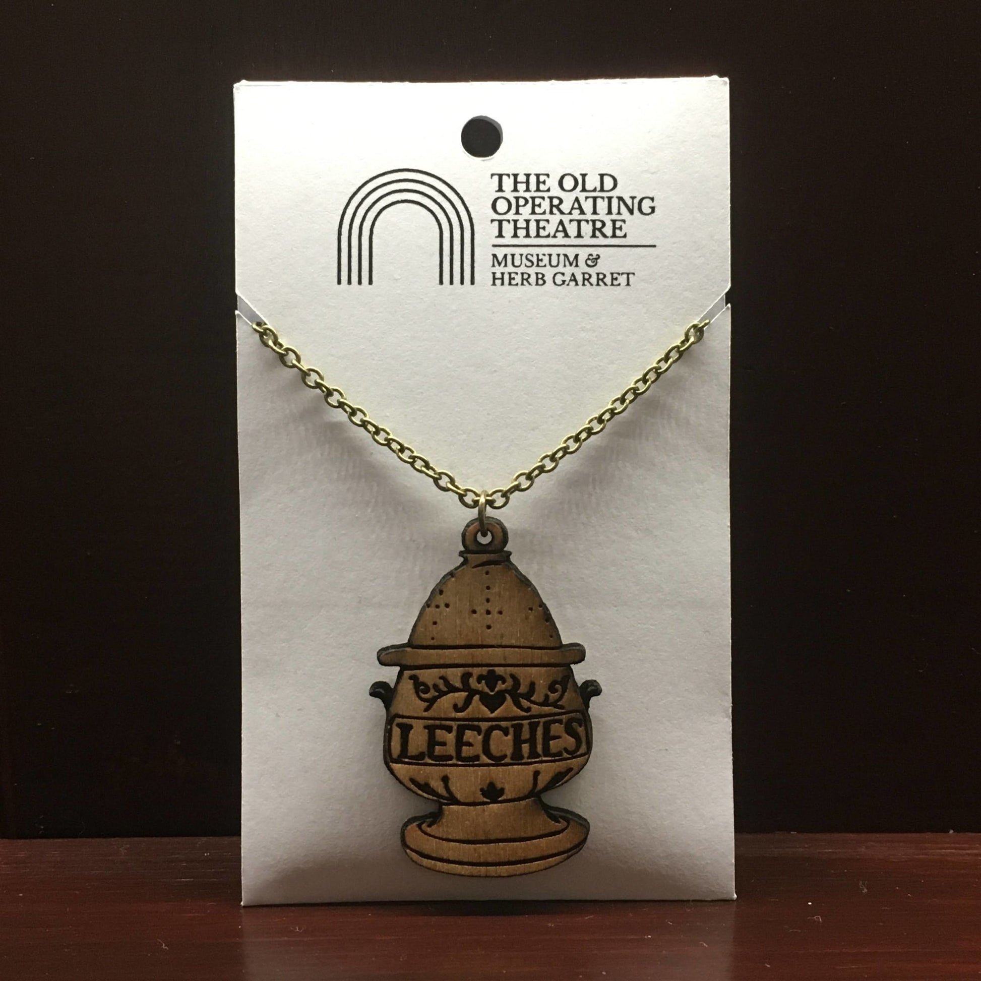 Wooden brooch in the form of an egg-shaped jar, with 'leeches' written across the centre, suspended from a metal chain