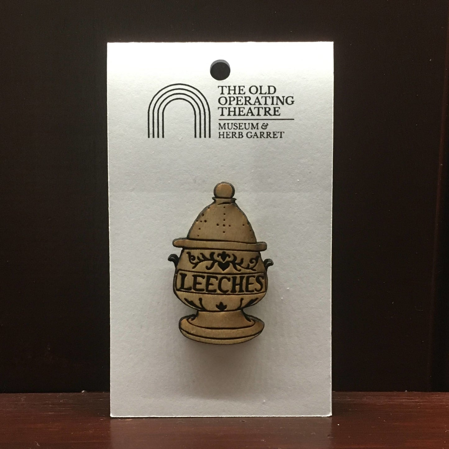 Egg-shaped wooden pendant designed as a jar with the word 'leeches' across the centre. Suspended on a metal chain.