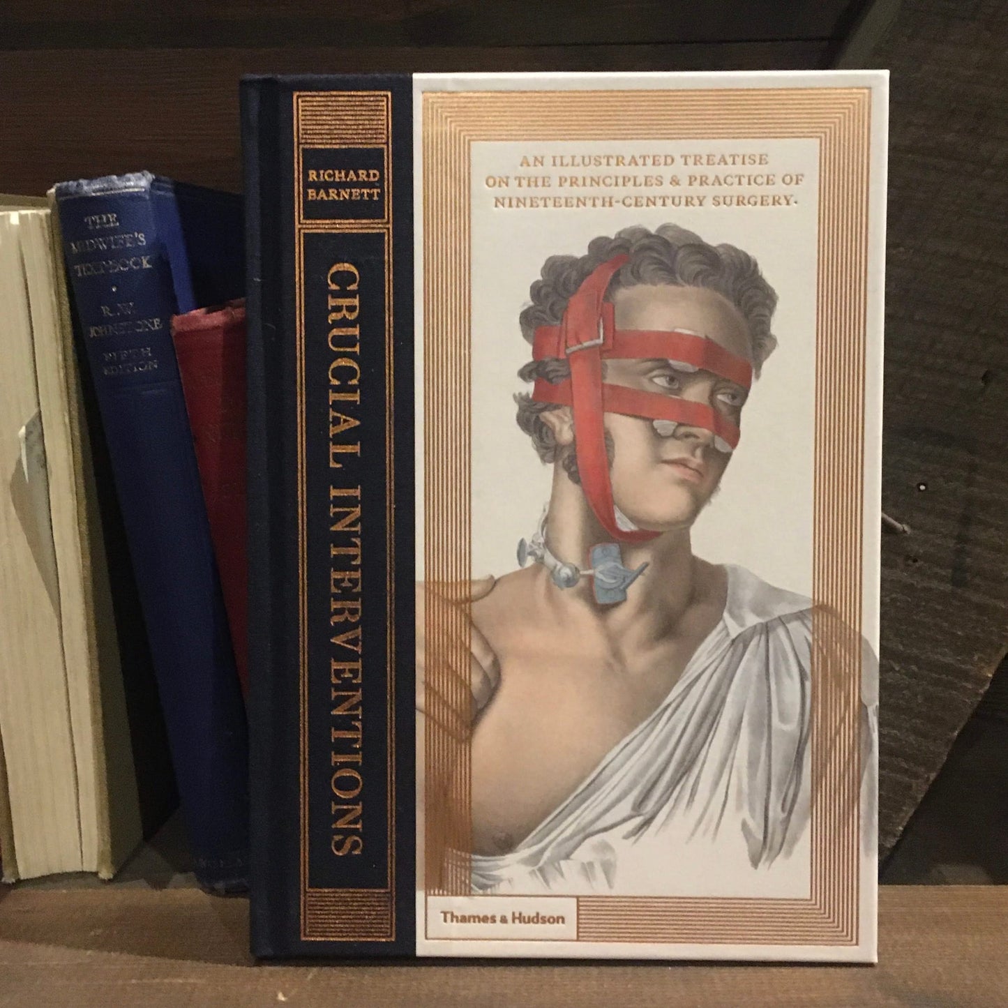 The hardback book Crucial Interventions on a shelf next to spines of hardback books