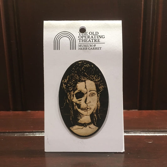 Wooden brooch with a woman's face that is half skull