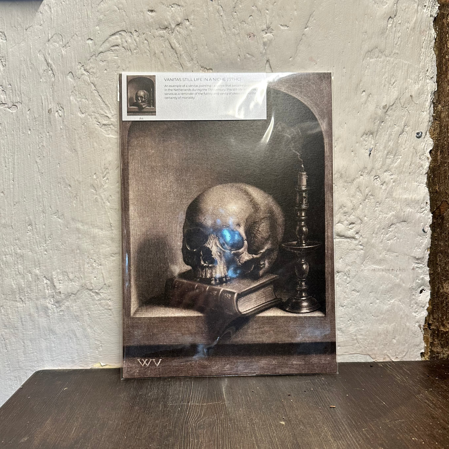 Artwork of a skull on a book with a candle, leaning against a textured wall.