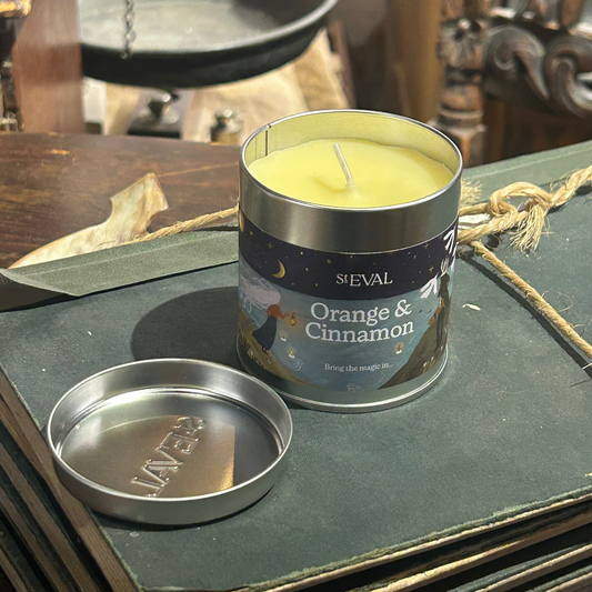 Candle in a metal tin labeled 'Orange & Cinnamon' by St. eval on a dark surface.