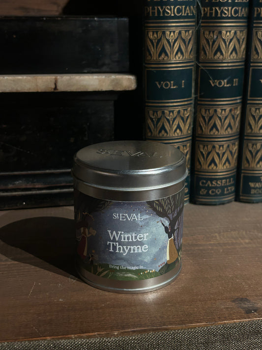 Seval Winter Thyme candle tin on a wooden surface with vintage books in the background