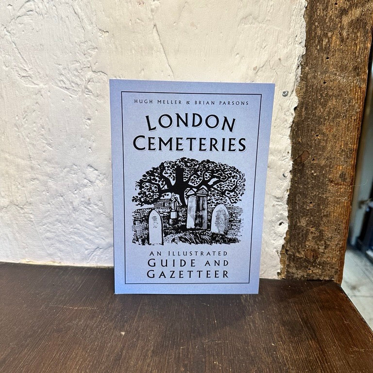 Book titled 'London Cemeteries' on a wooden surface with a textured white wall background