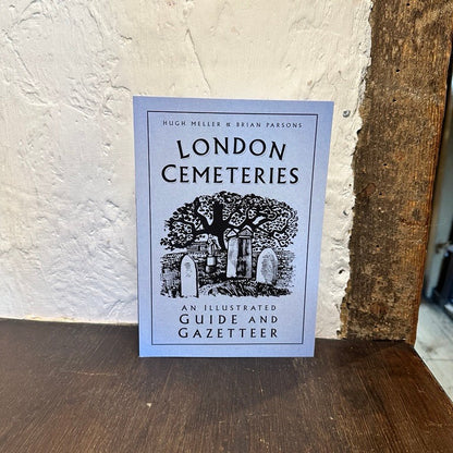 Book titled 'London Cemeteries' on a wooden surface with a textured white wall background