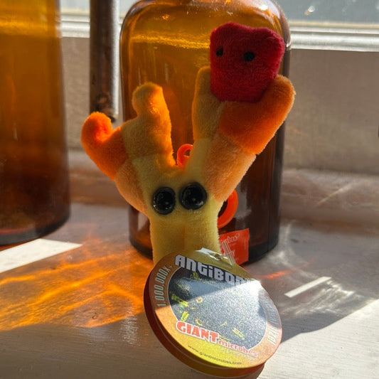 Small plush antibody keyring with googly eyes and an orange bottle in the background.
