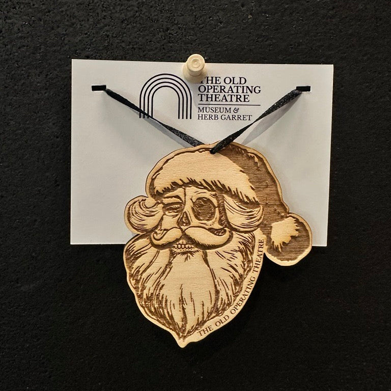 Wooden Santa Claus pendant on a card with 'The Old Operating Theatre Museum & Herb Garret' branding against a black background.