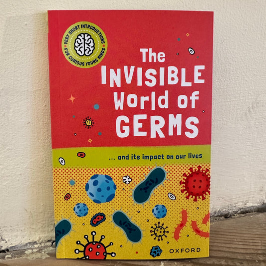 The book 'The Invisible World of Germs' by Oxford, featuring a red and yellow cover with illustrations of microorganisms, photographed leaning against a textured off-white wall.