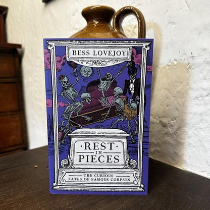 Book titled 'Rest in Pieces' by Bess Lovejoy on a wooden surface with a white textured wall in the background.