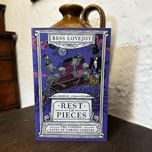 Book titled 'Rest in Pieces' by Bess Lovejoy on a wooden surface with a white textured wall in the background.