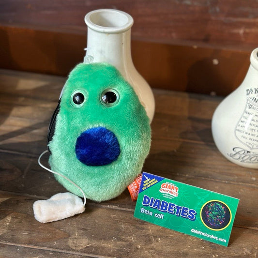 Green plush toy beta cell with a blue centre on a wooden surface with a card labeled 'Diabetes'.