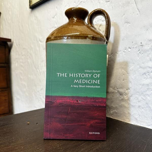 Book titled 'The History of Medicine: A Very Short Introduction' by William H. McKeown on a wooden surface with a ceramic jug.