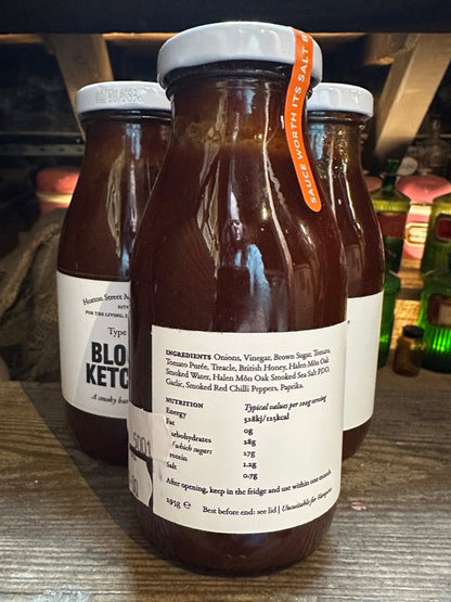 Three bottles of bloody ketchup on a wooden surface with a blurred background showing the ingredients list