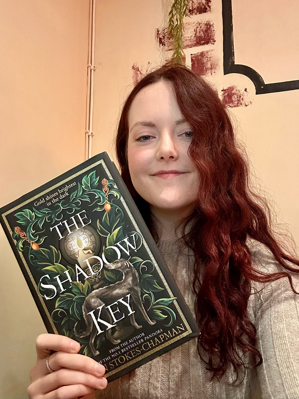 Colour selfie of a young woman holding a copy of The Shadow Key and smiling