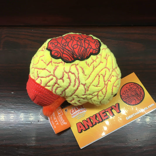 Yellow plush toy in the shape of a brain with a red cloud on its surface, on a wooden shelf
