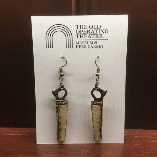 A pair of wooden earrings in the shape of a bone saw, hanging on a piece of white card with the museum's logo